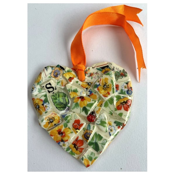 A heart shaped mosaic pendant with a wild flowers theme in orange and green.