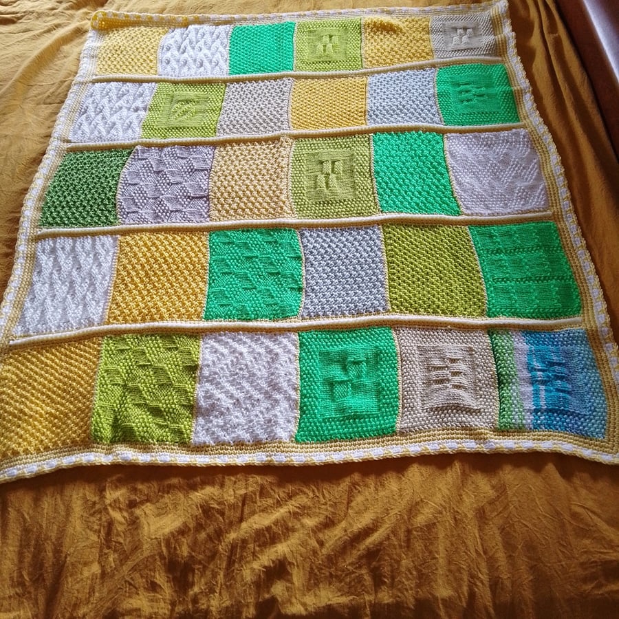 Baby or toddler handmade knitted blanket in a yellow and green theme.