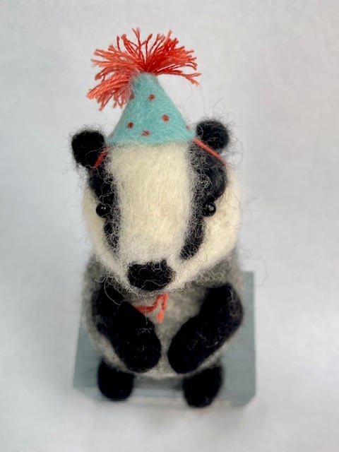 Handcrafted needle felted badger with removable party hat on a wooden box