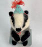Handcrafted needle felted badger with removable party hat on a wooden box