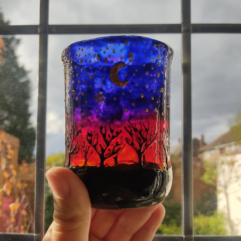 Handmade glass painted tea light candle holder with row of naked trees on sunset
