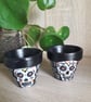 A pair of small terracotta plant pots handpainted with sugar skulls.  