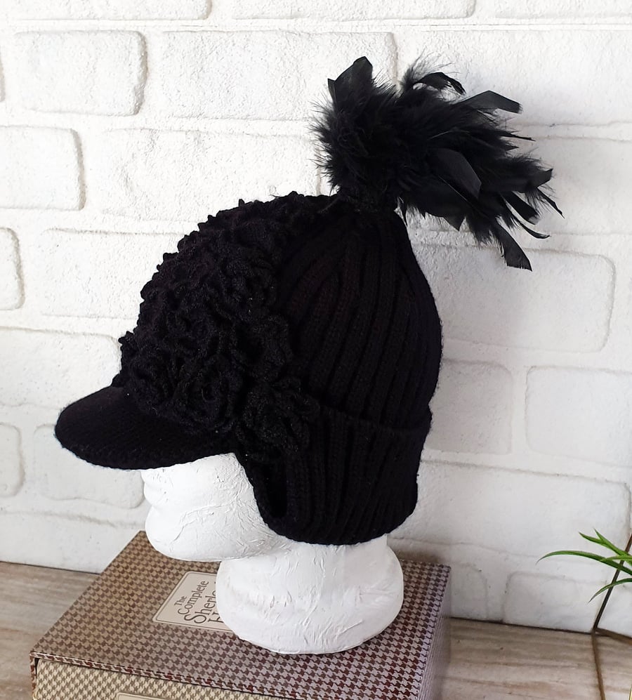Black helmet style crochet hat with black crochet flowers and feathered tail