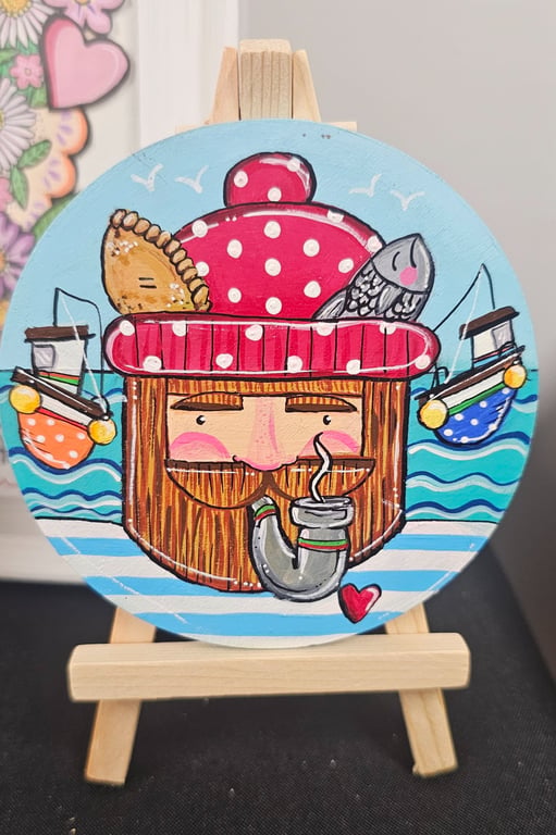 A fisherman painted on a wooden disc displayed on a little easel.