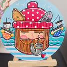 A fisherman painted on a wooden disc displayed on a little easel.