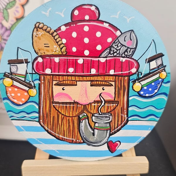 A fisherman painted on a wooden disc displayed on a little easel.