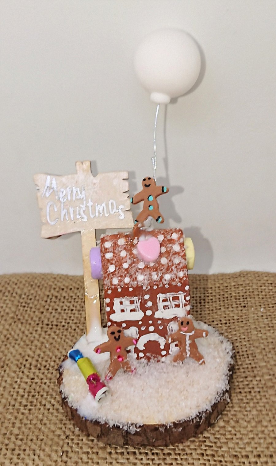 Small gingerbread house with gingerbread people snow scene on a log slice 