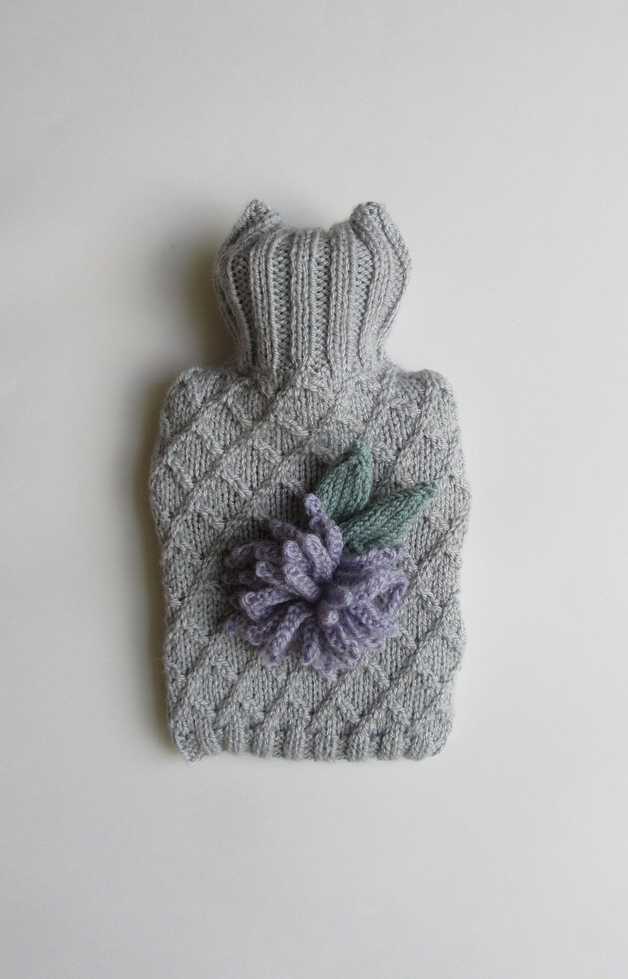 Hand knitted silver coloured hot water bottle with lilac allium flower