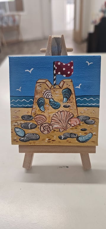 Cute little canvas of a sandcastle on a little easel.