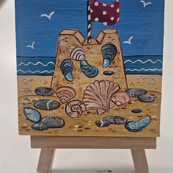 Cute little canvas of a sandcastle on a little easel.