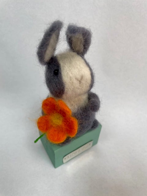 Handcrafted needle felted rabbit holding a flower on a wooden box