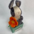 Handcrafted needle felted rabbit holding a flower on a wooden box