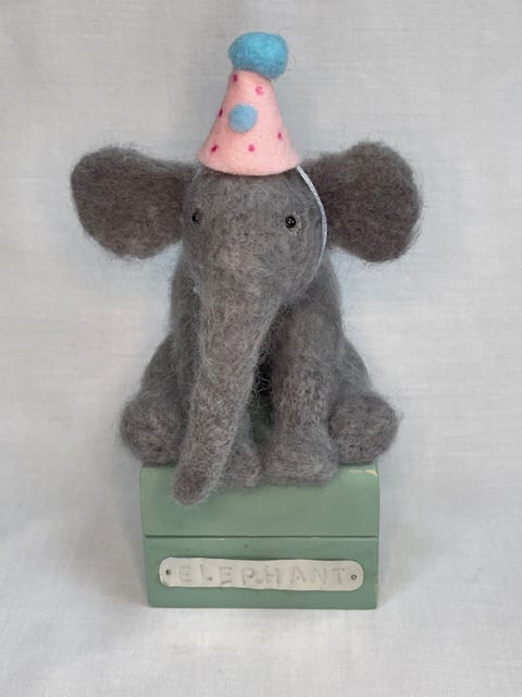 Handcrafted needle felted elephant with removable party hat on a wooden box