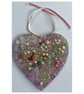 A wooden heart shaped pendant with a mauve theme and glass beads.