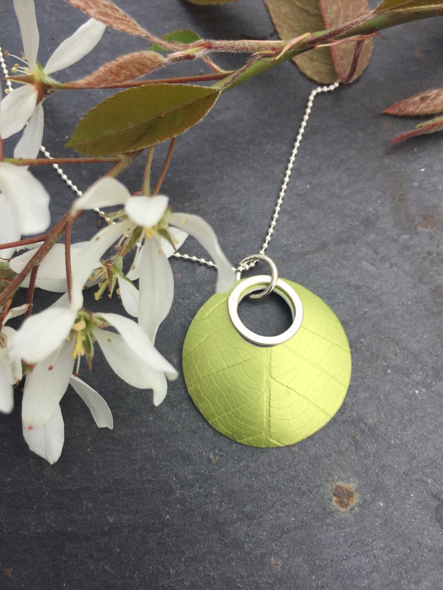 Circular anodised aluminium leaf textured pendant with silver ring.