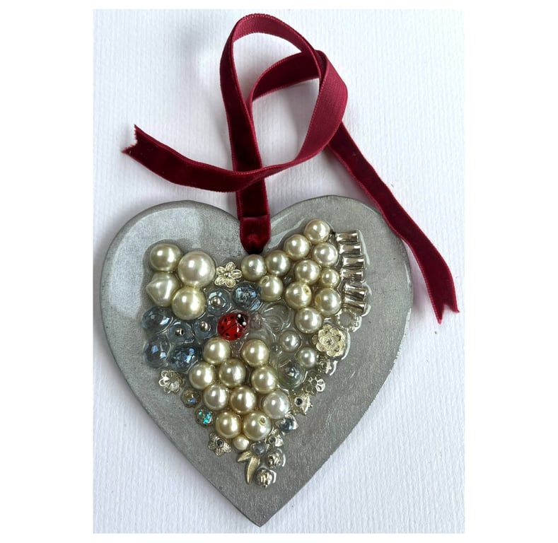 A wooden heart shaped pendant with pearly type and silver coloured shapes.