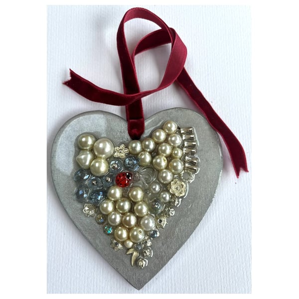 A wooden heart shaped pendant with pearly type and silver coloured shapes.