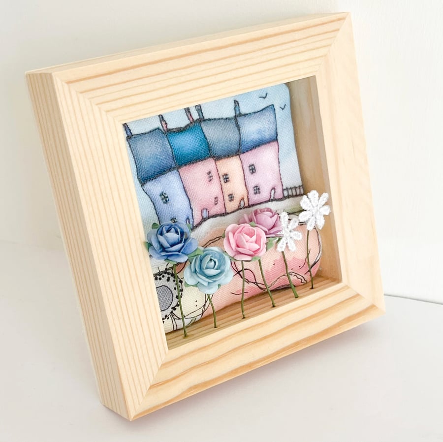 Little row of fabric houses with paper flowers, in a small wooden frame