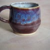 Pottery mug finished in a purple, blue glaze. Angular shape.