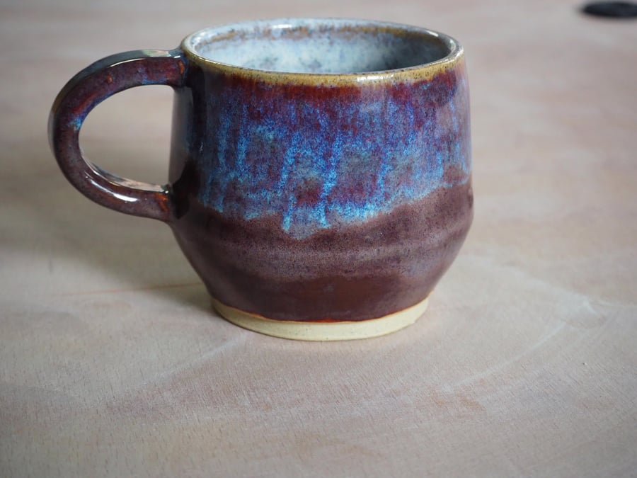 Pottery mug finished in a purple, blue glaze. Angular shape.