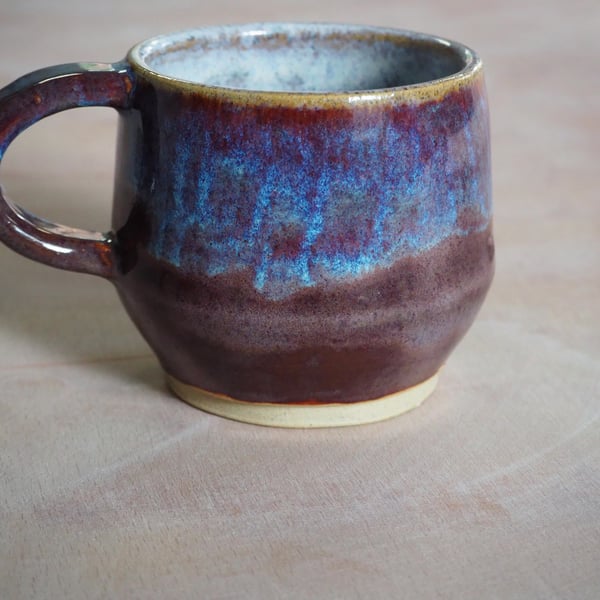 Pottery mug finished in a purple, blue glaze. Angular shape.