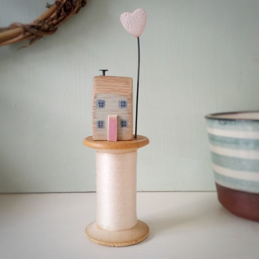 Tiny oak house with clay heart on vintage wooden bobbin