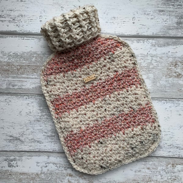 A hot water bottle and handmade crochet cover in red pink and cream tweed