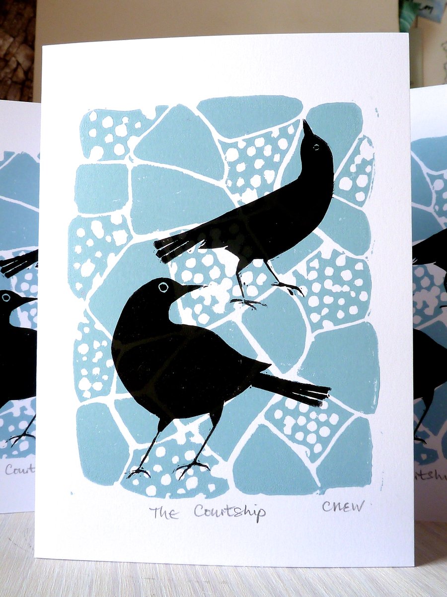 A lino cut greetings card of two blackbirds flirting on the crazy paving