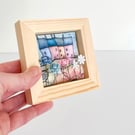 Little row of fabric houses with paper flowers, in a small wooden frame