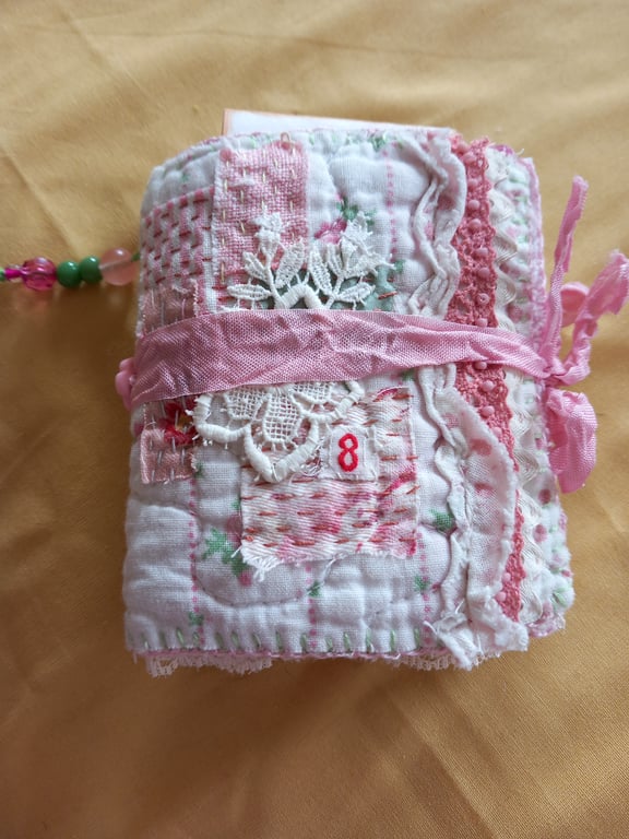 The pink and white needlecase, with pockets, pins, needles and  samples