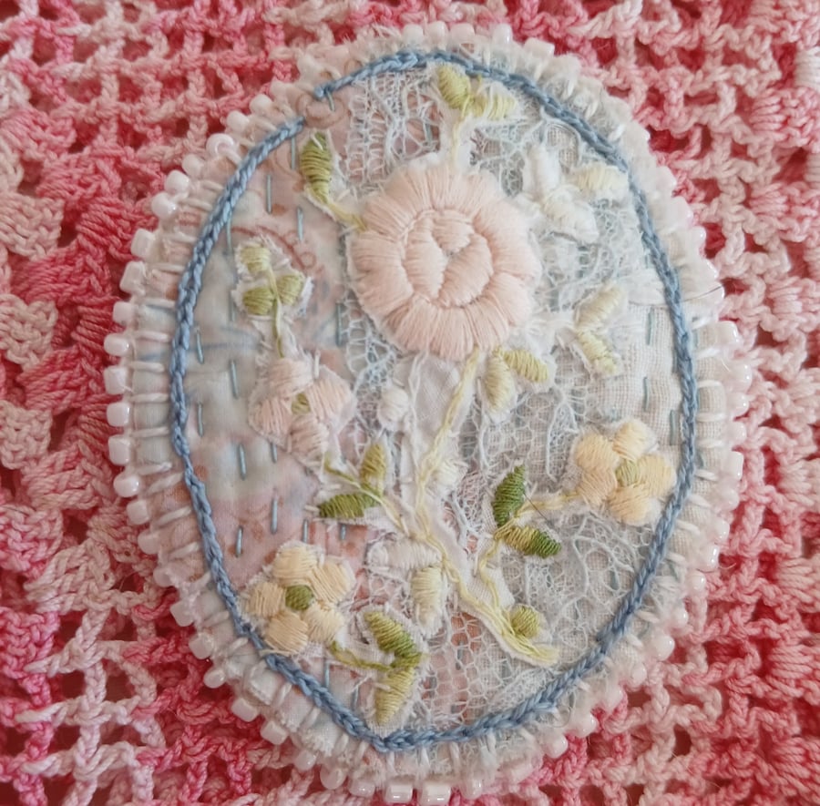 Oval, textile brooch with pastel, embroidered flowers.