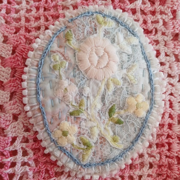 Oval, textile brooch with pastel, embroidered flowers.
