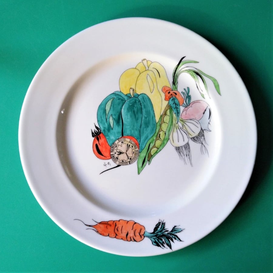 A large bone china dinner plate hand decorated with assorted vegetables.