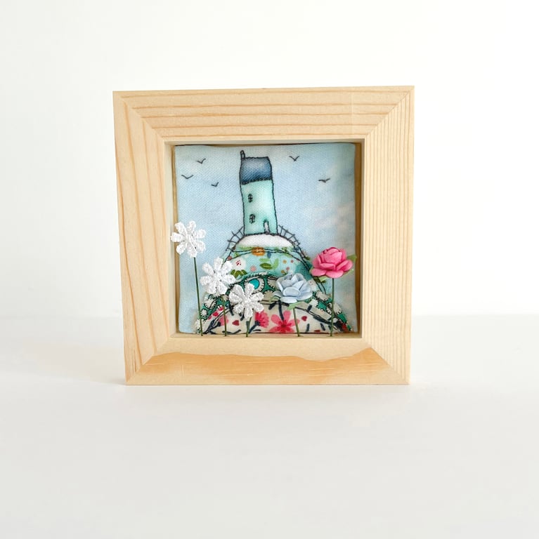 Little house on a fabric hill, with flowers, in small wooden frame