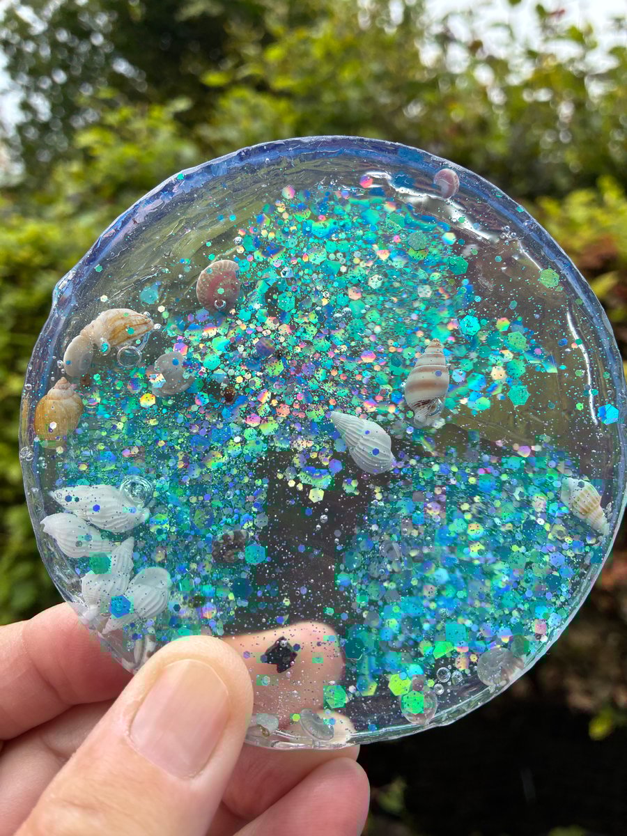 Resin coaster with teal blue green holographic glitter and tiny sea shells