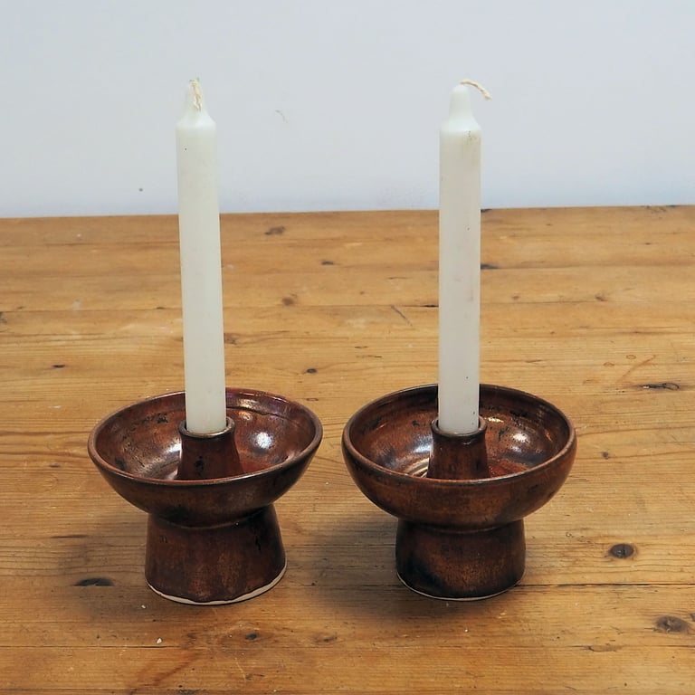 A pair of ceramic candlesticks in a rustic copper glaze