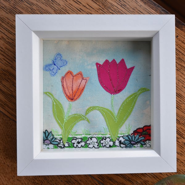 Box framed small applique of tulips on blue colourwash background.