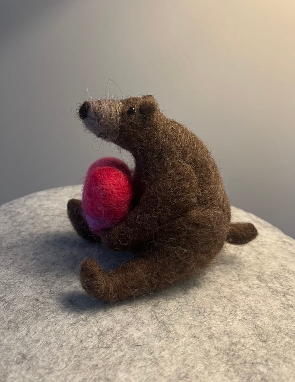 Needle felted bear holding a pink needle felted heart.