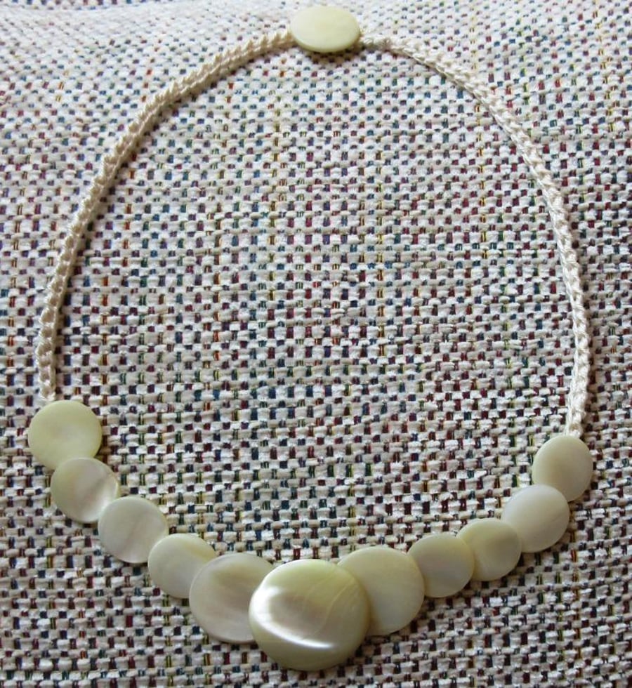 A button necklace comprising mother-of-pearl buttons on a crocheted chain