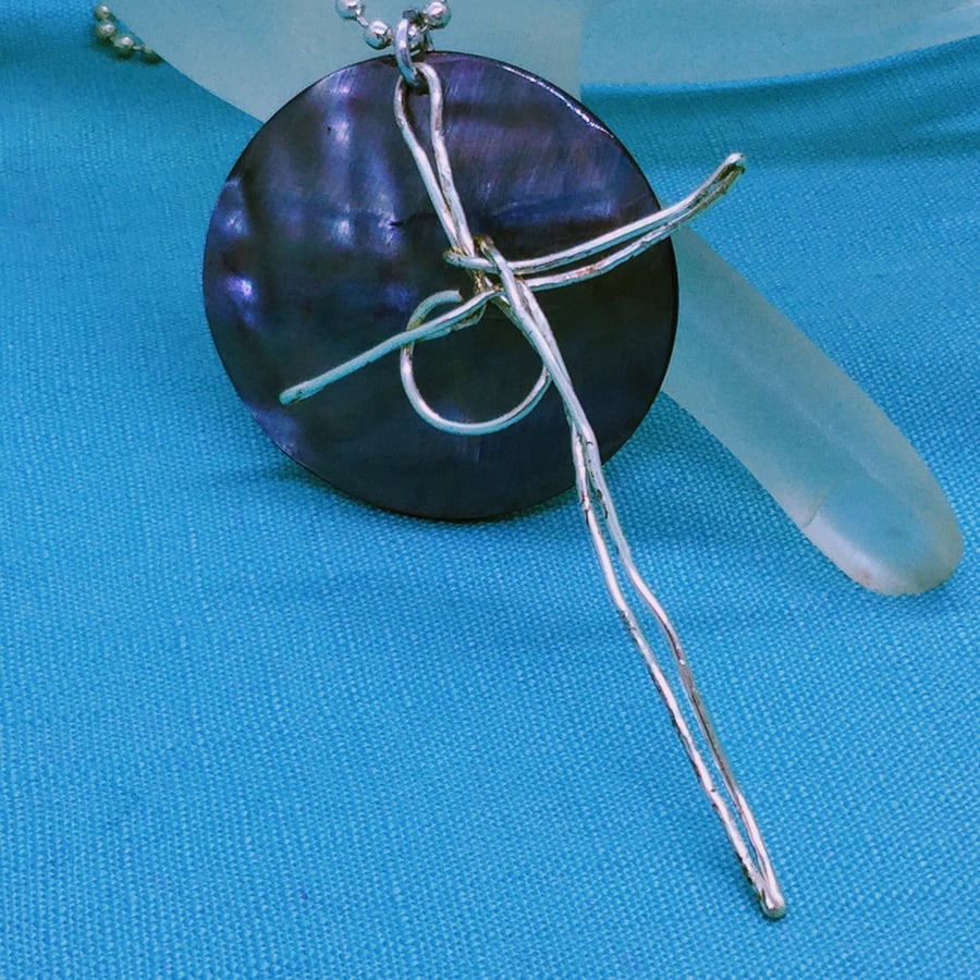 A Wearable Silver Meditational Cross On A Blue Shell Disc