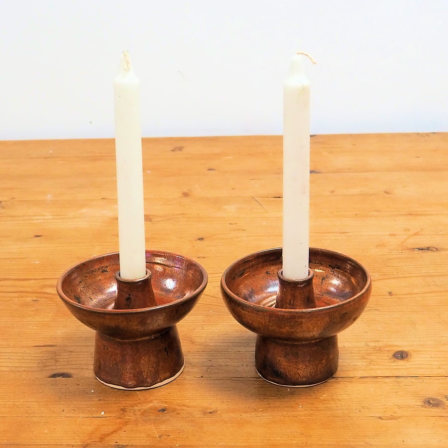 A pair of ceramic candlesticks in a rustic copper glaze