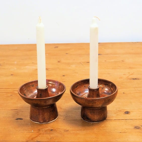 A pair of ceramic candlesticks in a rustic copper glaze