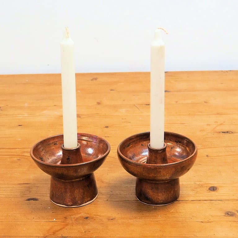 A pair of ceramic candlesticks in a rustic copper glaze