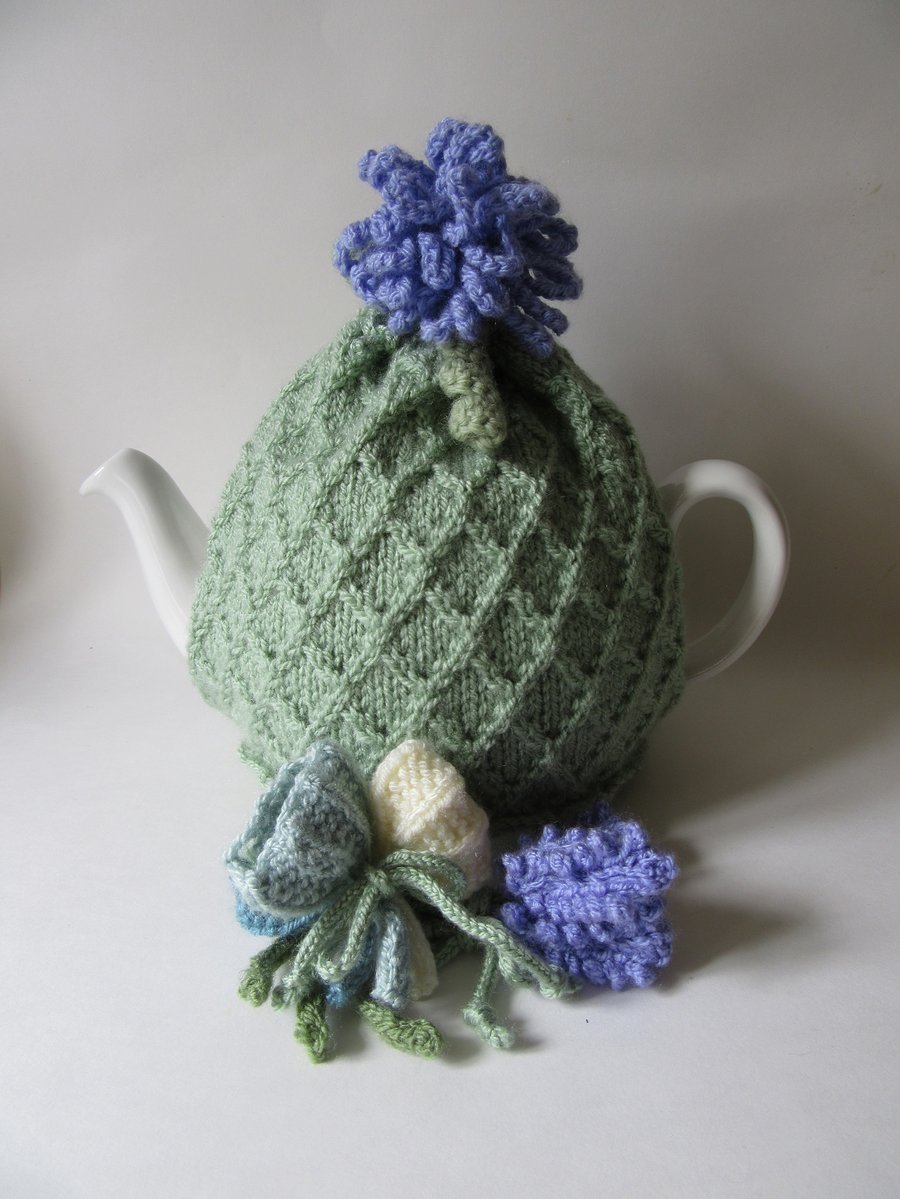 Hand knitted pastel green tea cosie with crocus, allium and lavender flowers
