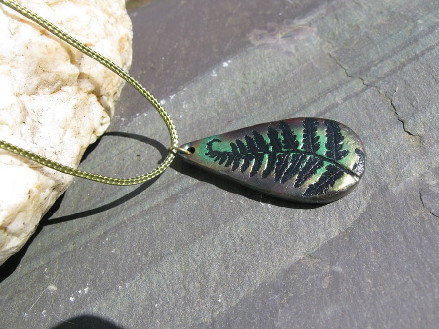 Metallic green and bronze fern tear-drop pendant on a green woven cord.