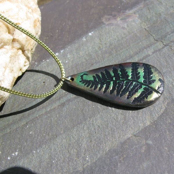 Metallic green and bronze fern tear-drop pendant on a green woven cord.