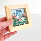 Fabric picture of houses and flowers, in a small wooden frame