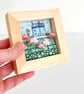 Fabric picture of houses and flowers, in a small wooden frame