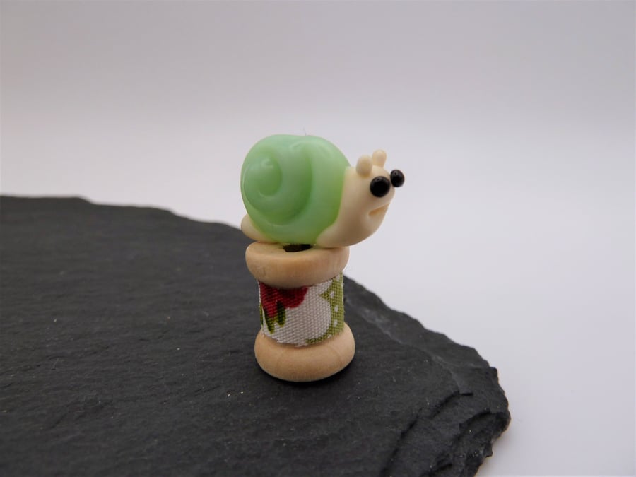 small glass snail on a wooden bobbin