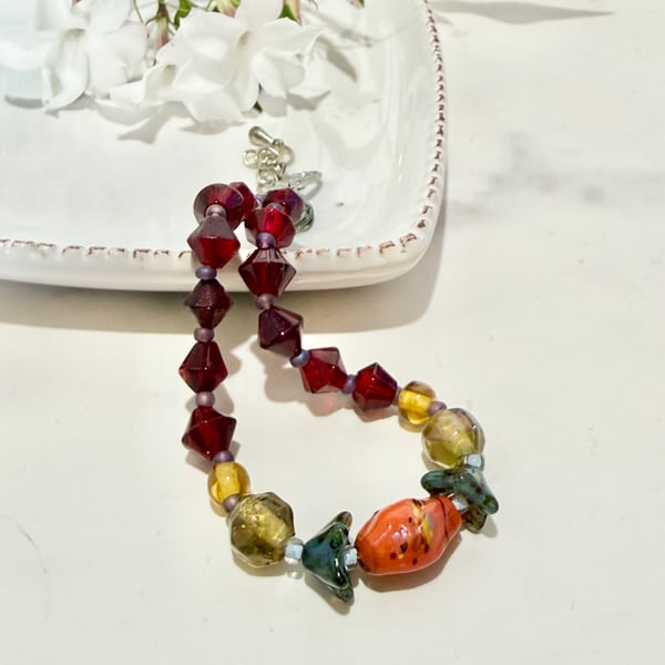 Slender glass bead bracelet in earthy shades of red and orange. 